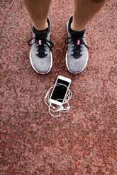 Lags eines jugendlichen Läufers mit Smartphone und Kopfhörern auf dem Boden liegend - GIOF04810