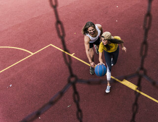 Young man and woman playing basketball on basketball ground - UUF15556