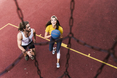Young man and woman playing basketball on basketball ground - UUF15557