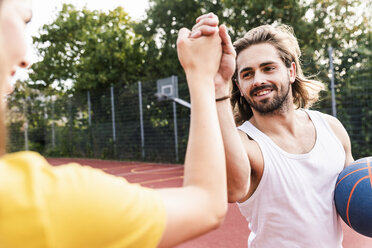 Young man and young woman high-fiving after basketball game - UUF15565