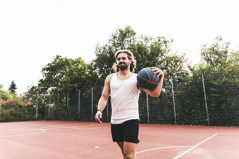 Junger Mann verlässt den Basketballplatz und trägt den Ball - UUF15567