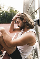Junger Mann sitzt müde und enttäuscht auf einem Basketballplatz - UUF15572