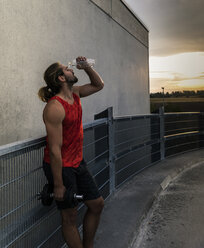 Junger Mann trinkt Wasser nach dem Training mit Hanteln - UUF15580