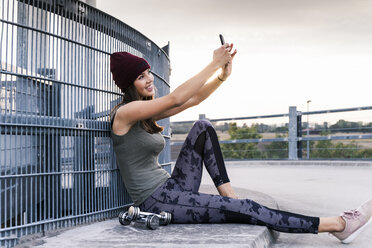 Junge Frau, die nach einem Hanteltraining auf dem Boden sitzt und ihr Smartphone benutzt - UUF15588