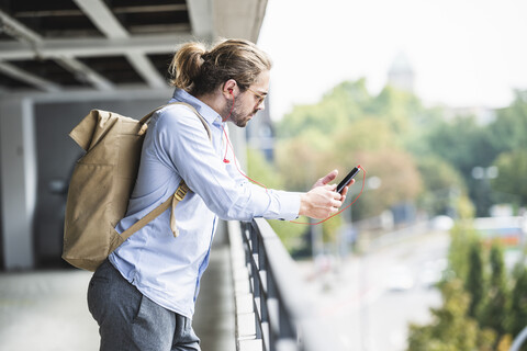 Junger Geschäftsmann mit Rucksack, in einem Parkhaus stehend, mit Smartphone, lizenzfreies Stockfoto