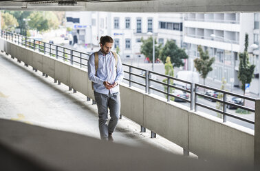 Young businessman walking in parking garage, using smartphone - UUF15617