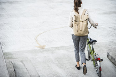 Junge Geschäftsfrau mit Rucksack, Fahrrad schiebend, Rückansicht - UUF15624