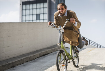 Laughing businessman riding down a ramp on his bicycle - UUF15629