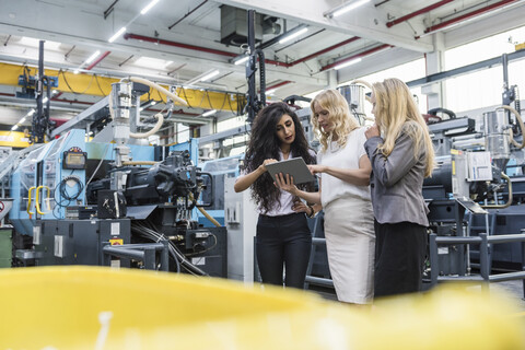 Drei Frauen mit Tablet im Gespräch in einer Fabrikhalle, lizenzfreies Stockfoto