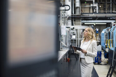 Frau mit Tablet an einer Maschine in einer Fabrikhalle und schaut sich um - DIGF05293