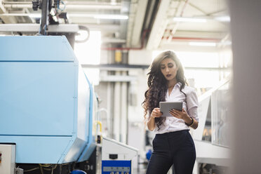 Woman using tablet at machine in factory shop floor - DIGF05308