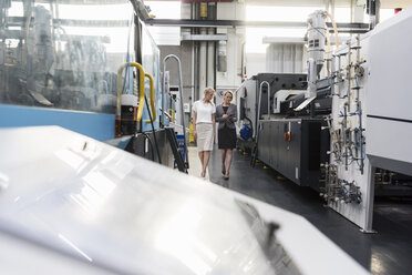 Two women with tablet walking and talking in factory shop floor - DIGF05315