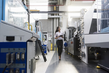 Frau mit Tablet an einer Maschine in einer Fabrikhalle, die sich umschaut - DIGF05317