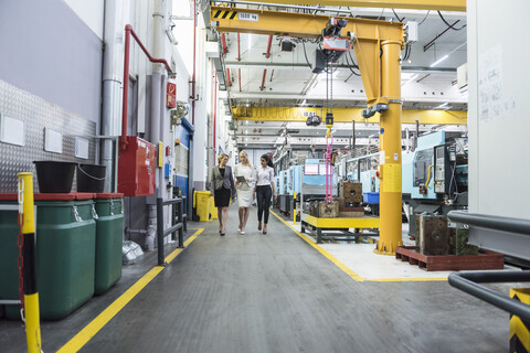 Drei Frauen mit Tablet gehen und sprechen in der Fabrikhalle, lizenzfreies Stockfoto