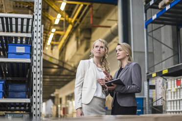 Zwei Frauen mit Tablet im Gespräch in einem Fabriklager - DIGF05334