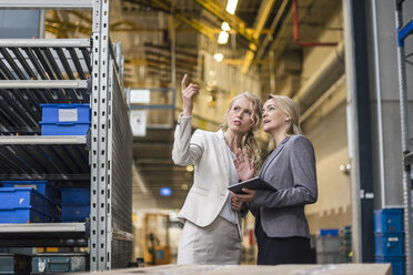 Zwei Frauen mit Tablet im Gespräch in einem Fabriklager - DIGF05335