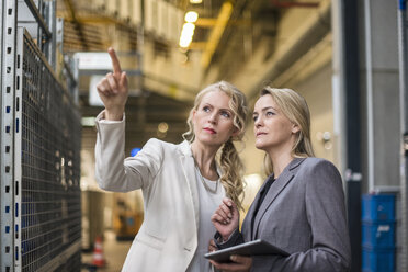 Zwei Frauen mit Tablet im Gespräch in einem Fabriklager - DIGF05336