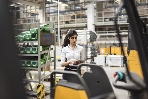 Frau benutzt Tablet in einer Fabrikhalle, lizenzfreies Stockfoto