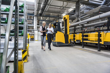 Zwei Frauen mit Tablet zu Fuß und im Gespräch in der Fabrik Shop Floor - DIGF05356