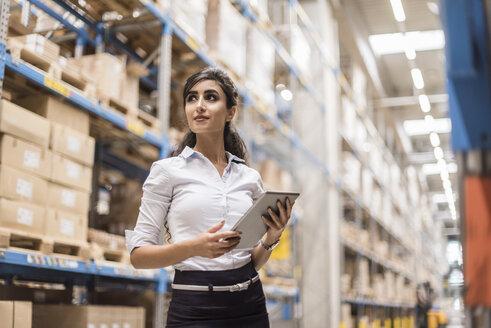 Woman with tablet in factory storehouse looking around - DIGF05367