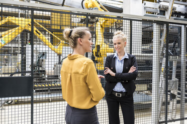 Two women talking in factory shop floor with industrial robot - DIGF05385