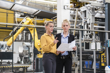 Two women discussing plan in factory shop floor with industrial robot - DIGF05390