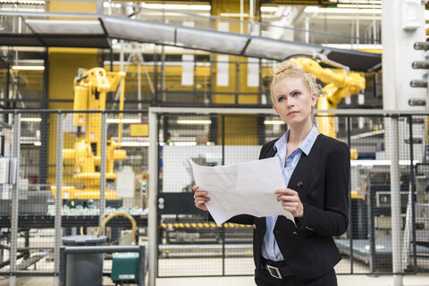 Woman holding plan in factory shop floor with industrial robot stock photo