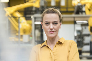 Porträt einer selbstbewussten Frau in einer Fabrikhalle mit Industrieroboter - DIGF05394