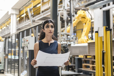 Woman holding plan in factory shop floor with industrial robot - DIGF05395