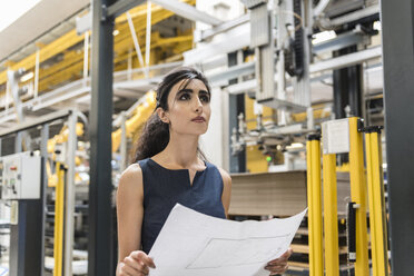 Woman holding plan in factory shop floor with industrial robot - DIGF05396