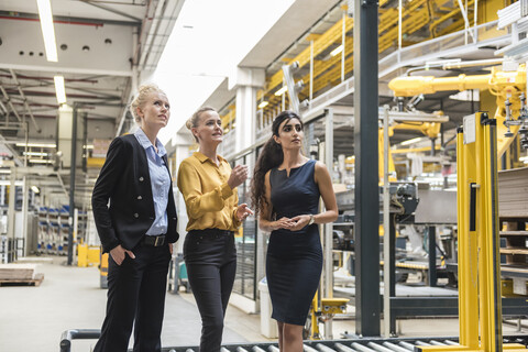 Drei Frauen im Gespräch in einer modernen Fabrik, lizenzfreies Stockfoto