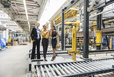 Three women discussing at conveyor belt in factory - DIGF05398