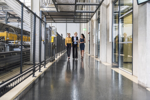 Three women with tablet walking and talking in factory shop floor stock photo