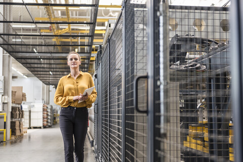 Frau mit Tablet zu Fuß in Fabrikhalle, lizenzfreies Stockfoto