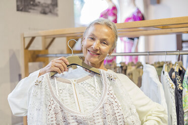 Porträt einer lächelnden älteren Frau, die in einer Boutique Kleidung einkauft - VGF00021