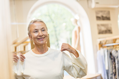 Lächelnde ältere Frau bei der Anprobe eines Pullovers in einer Boutique, lizenzfreies Stockfoto