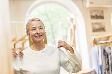 Lächelnde ältere Frau bei der Anprobe eines Pullovers in einer Boutique - VGF00026
