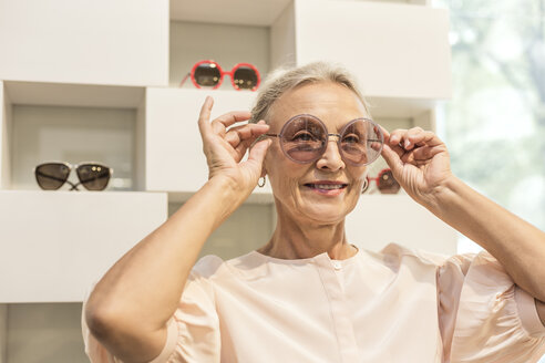 Smiling senior woman trying on sunglasses in a boutique - VGF00030