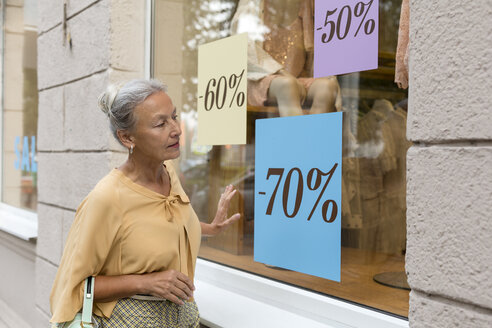 Ältere Frau schaut in das Schaufenster einer Boutique - VGF00038