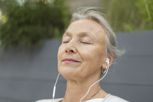 Porträt einer älteren Frau mit geschlossenen Augen und Kopfhörern im Freien - VGF00059