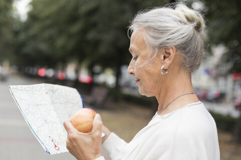 Ältere Frau im Freien mit Landkarte und Apfel, lizenzfreies Stockfoto
