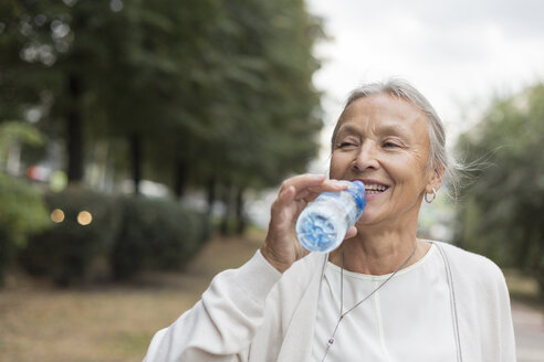 Glückliche ältere Frau im Freien, die Wasser aus einer Flasche trinkt - VGF00065