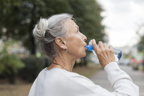 Ältere Frau trinkt im Freien Wasser aus einer Flasche - VGF00066