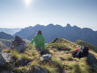 Italien, Lombardei, Bergamasker Voralpen, Wanderer sitzt auf dem Aussichtspunkt des Monte Gardena, Cima Bagozza im Gegenlicht - LAF02112