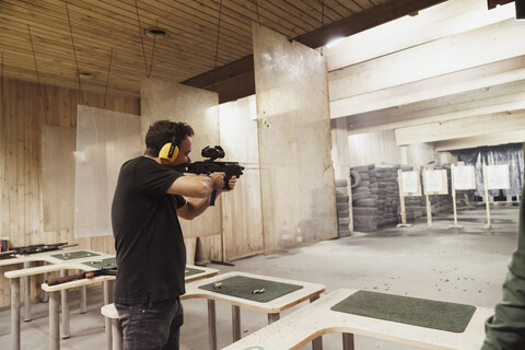 Mann zielt mit einem Gewehr in einer Indoor-Schießanlage, lizenzfreies Stockfoto