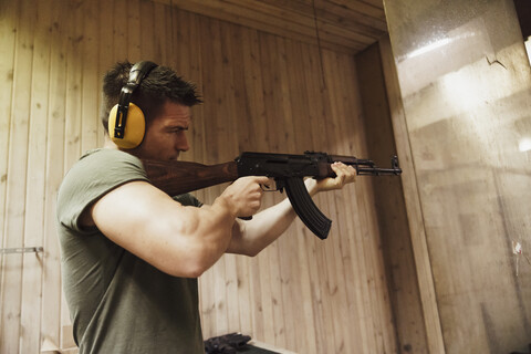 Mann zielt mit einem Gewehr in einer Indoor-Schießanlage, lizenzfreies Stockfoto