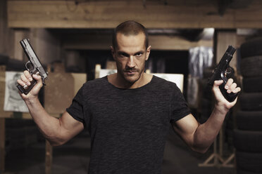 Portrait of man posing with two guns in an indoor shooting range - KKAF02597