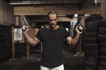 Portrait of man posing with two guns in an indoor shooting range - KKAF02598