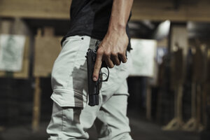 Close-up of man holding a pistol in an indoor shooting range - KKAF02600