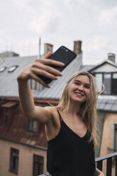 Porträt einer lächelnden blonden Frau, die ein Selfie auf der Dachterrasse macht - KKAF02626